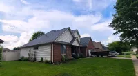 Suburban brick and siding homes with manicured lawns under a blue sky with scattered clouds.