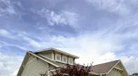Modern suburban house with new roof and trees under a partly cloudy blue sky with Roof It Forward logo.
