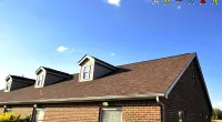 Red brick house with new brown roof shingles under clear blue sky and Roof It Forward logo.