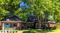 Brick house with a large front yard and trees with sunlight casting shadows on the lawn and facade.
