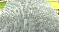 A gray asphalt shingle roof with a ridge running down the center, surrounded by green grass and a driveway.