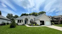 Modern single-story white brick house with a green lawn under a partly cloudy blue sky and Roof It Forward logo.