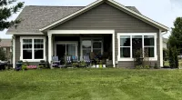 Single-story brown house with white trim, large windows, covered patio, and a well-maintained green lawn.
