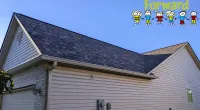 Residential house with new dark shingle roof under clear blue sky and Roof It Forward logo with children icons.
