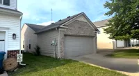 Detached two-car garage with brick and siding exterior next to lawn and driveway under blue sky.