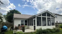 Backyard view of a house with a screened porch, patio furniture, green lawn, and blue sky with clouds.