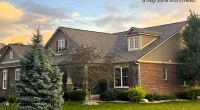 Suburban house with brick facade, dormer windows, and green lawn under a partly cloudy sunset sky