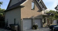 Two-story suburban house with brick and siding exterior, double garage doors, and driveway under a clear sky.