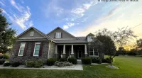 Stone and siding house with porch at sunset under a partly cloudy sky and text Roof It Forward charity logo