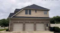Suburban two-story house with three-car garage and pitched roof under a cloudy sky