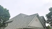 Residential house with new gray shingle roof and white truck parked in front on cloudy day