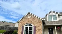 Brick and siding house with purple shutters and door under a bright blue partly cloudy sky.