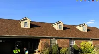 Brick house with a brown shingle roof, three dormer windows, and a clear blue sky background.