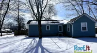 Blue house in snowy yard with bare trees casting shadows on the snow under a bright blue sky