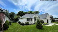 Suburban house with freshly renovated roof, green lawn, and bright blue sky with clouds above