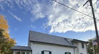 White two-story house with new gray shingle roof and clear blue sky with clouds overhead