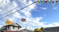 Suburban homes under a partly cloudy sky with an American flag on a pole and power lines overhead.