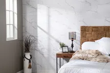 Thumbnail for Bright bedroom corner with wicker headboard, white bedding, wooden nightstand, lamp, and decorative vase by window