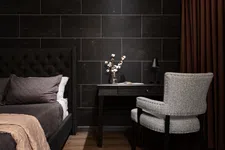 Thumbnail for Modern bedroom corner with dark tiled wall, upholstered bed, black desk, gray chair, and brown curtains.