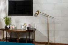 Thumbnail for Modern bedroom corner with wall-mounted TV, wooden console table, gold floor lamp, and decorative plants and books.