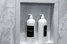 Thumbnail for Two white pump bottles of shampoo and conditioner in a recessed marble shower niche.