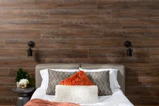 Thumbnail for Cozy bed with textured pillows and throw against a dark wooden plank accent wall with wall-mounted lamps.