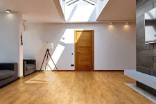 Thumbnail for Bright modern living room with wooden flooring, skylight, wooden door, gray sofas, and a tripod floor lamp.