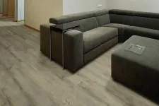 Thumbnail for Modern living room with gray sectional sofa, dark ottoman, and light wood laminate flooring under soft lighting.