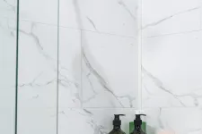 Thumbnail for Modern showerhead with glass shower screen, marble wall tiles, green soap dispensers, and a folded towel on a rack.