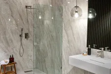Thumbnail for Modern bathroom with glass shower enclosure, marble walls, floating sink, pendant light, and wooden stools.