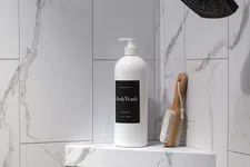 Thumbnail for White body wash bottle and wooden brush on marble shower shelf under black showerhead in modern bathroom