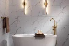 Thumbnail for Modern bathroom with freestanding white tub, gold faucet, marble walls, candle tray, and sculptural wall lights.