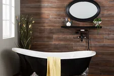 Thumbnail for Black clawfoot bathtub with yellow towel in a rustic bathroom featuring wood wall tiles and oval mirror