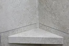 Thumbnail for Triangular stone corner shelf mounted on beige tiled wall with subtle texture and grout lines