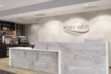 Thumbnail for Modern hotel reception desk with marble finish and coffee bar in the background under recessed lighting.