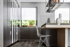 Thumbnail for Modern kitchen with sleek gray cabinets, wooden flooring, metal wire chair, and minimalist decor under natural light.