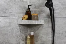 Thumbnail for Modern shower corner with black showerhead and shelves holding toiletries in a gray tiled bathroom.