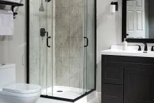Thumbnail for Modern bathroom with glass shower enclosure, black vanity, toilet, and neutral tile flooring and walls.