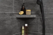 Thumbnail for Modern corner shower shelves with bottles and jars against dark gray tiled bathroom walls.