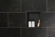 Thumbnail for Two white pump bottles and a wooden brush in a black tiled shower niche with dark grout lines.