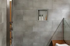 Thumbnail for Modern shower area with gray tiled walls, built-in soap niche, wooden bench, and folded towels on bench.