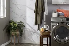 Thumbnail for Modern laundry room with front-load washer, hanging robes, wicker plant stand, and folded clothes on cabinet