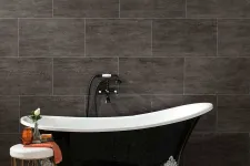 Thumbnail for Black clawfoot bathtub with silver feet against dark tile wall and decorative stool with orange towel and vase