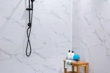Thumbnail for Modern shower with black fixtures and marble wall tiles next to a wooden stool with toiletries and a blue sponge.