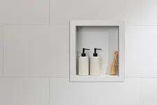 Thumbnail for White tiled bathroom wall with recessed shelf holding two white pump bottles and a wooden brush.