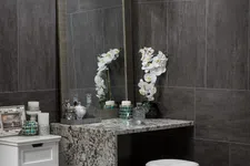Thumbnail for Modern vanity area with granite countertop, large mirror, white orchid, candles, and decorative items in gray tiled room