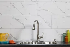 Thumbnail for Modern kitchen sink with stainless steel faucet, black countertop, white marble backsplash, and colorful jars.