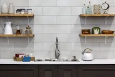 Thumbnail for Modern kitchen sink with dark cabinets, floating wooden shelves holding glassware, mugs, and decorative items.