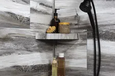 Thumbnail for Modern shower corner with gray marble tiles, black showerhead, and shelves holding bath products and brush.
