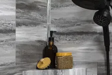 Thumbnail for Modern bathroom shower with dark showerhead, gray marble tiles, soap dispenser, scrub brush, and exfoliating scrub jar.